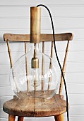 Retro pendant lamp with glass lampshade on nostalgic wooden chair against white wooden wall