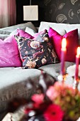 Graues Polstersofa mit pinkfarbenen Kissen und romantischem Kerzenlicht im Vordergrund