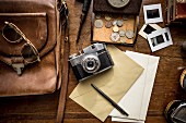 Stillleben mit Vintage Objekten; Fotoapparat, Ledertasche, Münzen und Schreibutensilien auf Holzunterlage