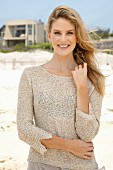 A young blonde woman on a beach wearing a beige knitted jumper