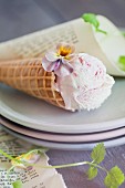 Strawberry ice cream in a cone decorated with pansies on a stack of plates