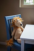 Soft toy sitting on child's chair at table below window