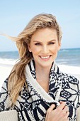 A young blonde woman on a beach wearing a blue-and-white patterned knitted cardigan with a shawl collar