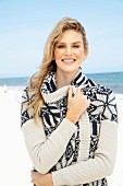 Junge, blonde Frau am Strand mit weiss-blau gemusterter Strickjacke mit Schalkragen