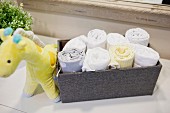 Aufgerollte Handtücher in stoffbezogener Box daneben Stofftier