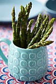 Cooked green asparagus in a light blue, ceramic mug