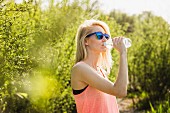 Junge blonde Frau im Park trinkt aus Wasserflasche