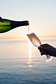 Champagner wird in Flöte vor Sonnenuntergang am Meer gegossen
