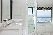 Luxuriöses Badezimmer in Weiß mit Waschtisch, abgetrenntem Duschraum und Badewanne mit Blick aufs Meer