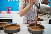 A woman pouring cake mixture into cake tins in a bakery