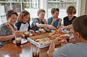 Group of boys eating pizza from boxes at a kitchen table