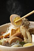 Chopsticks holding a slice of hard-boiled egg from a bowl of oriental noodle soup