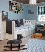 Rocking sheep next to pastel blue and white checked rug in front of white single bed with tall backrest, foot and headboard