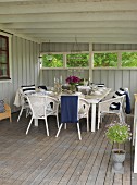 Gedeckter Tisch und weiße Rattanstühle auf Holzboden einer Loggia