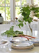 Flea market crockery and glasses, rhubarb and lilac on white dining table