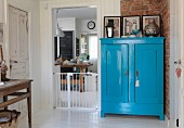 Blue-painted farmhouse cupboard against brick wall next to baby gate in kitchen doorway