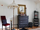 Gilt-framed mirror above chest of drawers, antique chair and decorative parasol in bedroom