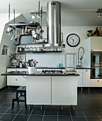 Extractor tube and cooking utensils hanging from grille above island with cooker in black and white, modern kitchen