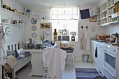 Vintage kitchen with sales table, tea towels hung in front of window, decorative plates and shelves of crockery on walls