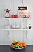 Sign with motto, scales and favourite crockery on white shelves above bowl of fruit in Scandinavian country-house kitchen