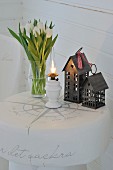 Vase of tulips, oil lamp and miniature house on white-painted tree stump stool with decorative lettering
