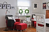 Interior in Scandinavian country-house style with red armchairs, white-painted wooden furniture and snaking standard lamp