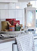 Dish of storage tins, tea towel and vintage-style, white-painted lantern on kitchen counter