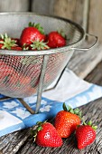 Frische Erdbeeren auf Holztisch in Metallsieb und daneben