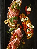 Bruschetta topped with tomatoes, fresh herbs, salami, prosciutto and mozzarella