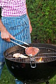 A man turning salmon fillets on a kettle barbecue
