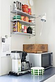 Microwave, coffee machine and bowl on kitchen worksurface; vintage toaster and clip-on lamp on wall-mounted shelves in corner of retro kitchen