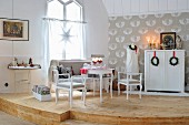 Romantischer, weisser Shabby-Sitzbereich auf einem gerundeten Holzpodest; Deko mit weihnachtlichen Kränzen an roten Bändern