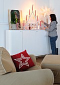 Festive arrangement on sideboard with woman lighting candles behind cushion with star motif on armchair