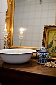 Vintage metal wash basin and chine pot with lid in front of gilt-framed mirror