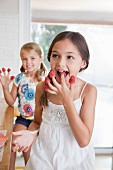 Two sisters with raspberries on their fingers in a kitchen