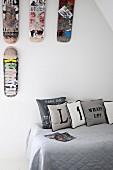 Scatter cushions printed with letters on grey throw on teenager's bed below scuffed skateboards decorating wall