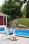 White chair on wooden deck next to pool with garden view