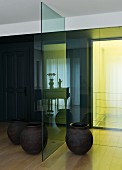 Simple floor vases either side of glass partition, yellow light streaming into foyer