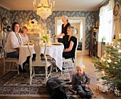 Toddler and dog sitting on rug next to Christmas tree in front of family around dinner table in traditional dining room