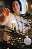 Woman decorating Christmas tree - candle-shaped fairy lights and baubles on branches