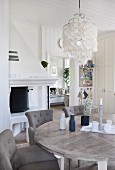Dining area with grey, upholstered chairs around wooden table below pendant lamp with capiz shell lampshade in rustic interior