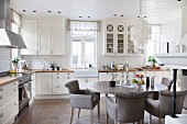 Comfortable dining area with grey upholstered chairs and oval dining table in white country-house kitchen