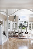 Elegant dining room with antique chairs around long table; foot of staircase and white, wooden column in foreground