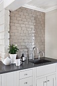 Kitchen counter with sink, black worksurface and pale grey, tiled splashback