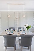 Chairs with grey upholstery at set table below two pendant lamps