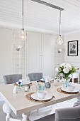 Vase of flowers on set table below pendant lamps