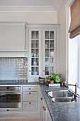 Corner of kitchen with country-house-style, glass-fronted cabinets and sink with vintage tap fittings