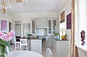 Dining set in open-plan, country-house kitchen with pale grey fronts and bar stools around island counter