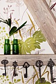 Vintage Schlüsselsammlung an Fachwerkbalken aufgehängt und grüne Glasvasen vor Tapete mit Blättermotiv