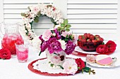 Drinks, berries & biscuits on table decorated with wreath of roses & vase of peonies